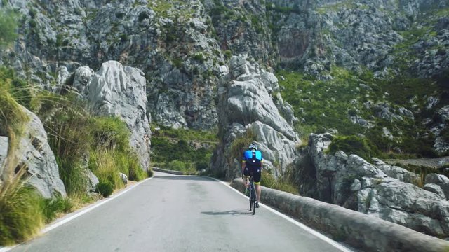 Point of view shot of a driver in his car driving along a straight section of Serra de Tramuntana Road towards Sa Calobra in Majorca, overtaking a cyclist to his right.