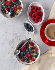 Flat lay coffee, bowl of oat flakes with blueberries and raspberries on concrete background.