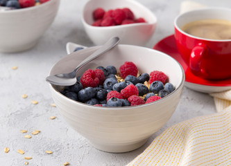 Coffee, bowl of oat flakes with blueberries and raspberries on concrete background.