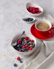 Coffee, bowl of oat flakes with blueberries and raspberries on concrete background.