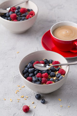 Coffee, bowl of oat flakes with blueberries and raspberries on concrete background.