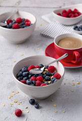 Coffee, bowl of oat flakes with blueberries and raspberries on concrete background.