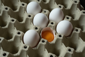 Half cracked egg in the paper egg tray. Egg yolk in egg shell. White eggs