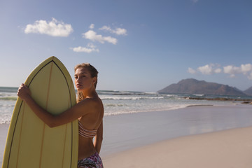 Female surfer standing with surfboard at beach