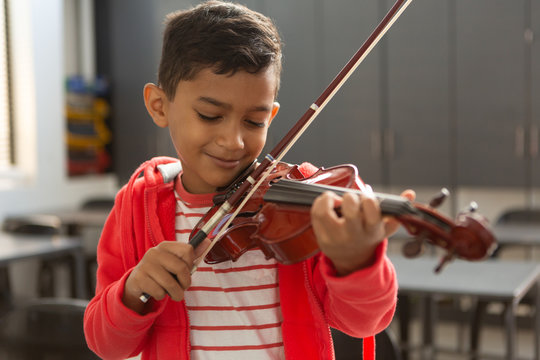 Smiling schoolboy with eyes closed playing violin in classroom