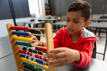 Schoolboy learning math with abacus at desk in a classroom