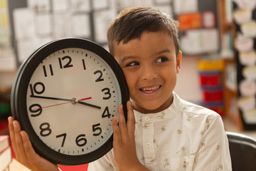 Smiling schoolboy with wall clock looking away in a classroom