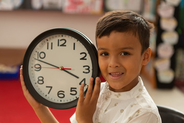 Smiling schoolboy with wall clock looking at camera in a classroom