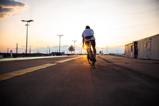 A Man Ride A Bicycle At Sunset With Sunbeam Over Urban Landscape, Road