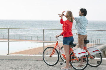 Caucasian couple interacting with each other while holding bicycle at promenade