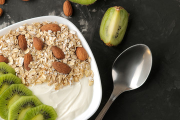 Greek white yogurt with kiwi almonds and oatmeal on a dark graphite table. breakfast. top view. healthy food
