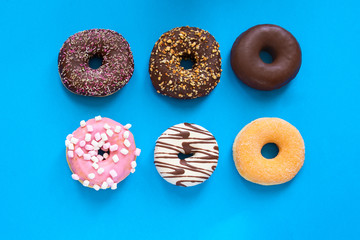 Different donuts with  chocolate frosted, pink glazed and sprinkles on blue lbackground with copy space. Assortment of  various colorful donuts. Top view
