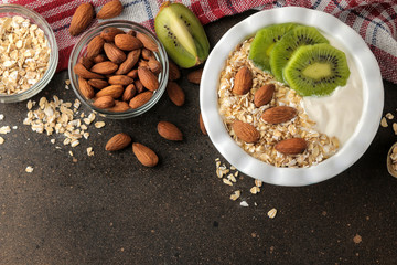 Greek white yogurt with kiwi almonds and oatmeal on a dark brown table. breakfast. top view. healthy food
