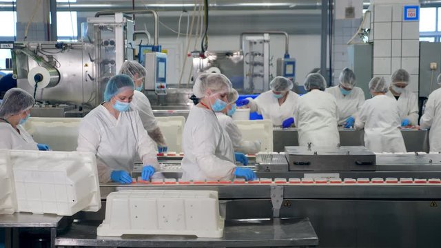Female workers are displacing pieces of packed snacks on a food factory conveyor.