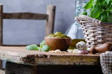 Pesto sauce in a olive wooden bowl with pine nuts, basil, parmesan and garlic over rustic table.