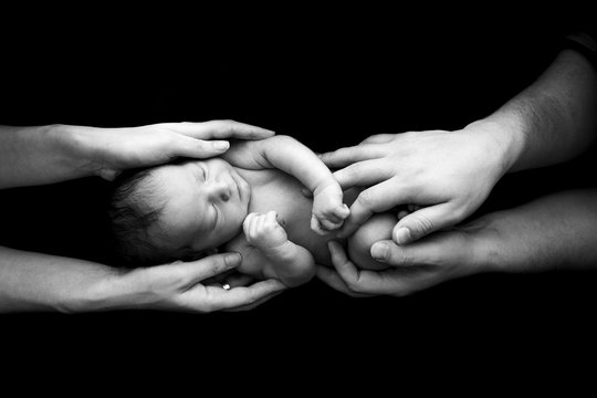 Parents hold their newborn son in their arms. Picture taken on a dark background.