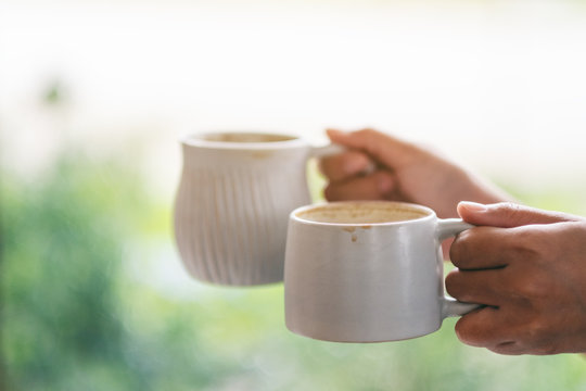 Closeup image of hands holding two white cups of hot coffee with blurred nature background