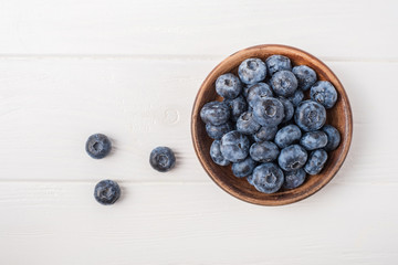 Blueberries in small clay bowl on white wooden table.