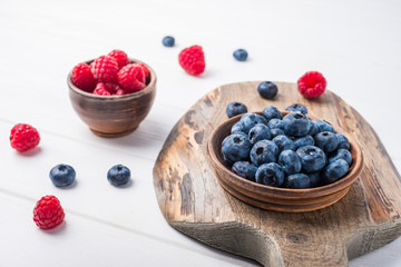 Raspberries and blueberries in small clay bowls on wooden board and table.