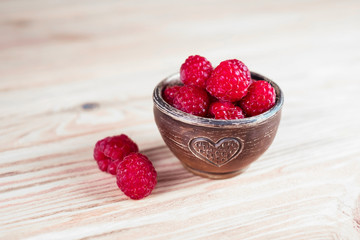 Raspberries in small clay bowl with heart image on wooden background