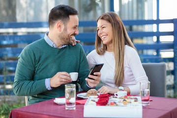 Smiling happy millennial couple celebrating anniversary or birthday in a restaurant. Eating cake and drinking coffee.