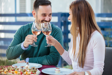 Smiling happy millennial couple celebrating anniversary or birthday in a restaurant. Making a toast, drinking wine and eating snacks