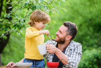 Obraz premium Food habits. Little boy with dad eating food nature background. Summer breakfast. Healthy food concept. Father son eat food and have fun. Feeding baby. Menu for children. Family enjoy homemade meal