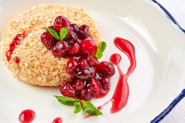 baked camembert with cranberry jam and mint leaves at white wooden table top. fried camembert with berry sauce is traditional french cuisine dessert