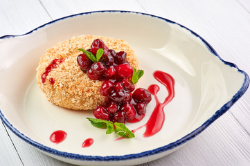 baked camembert with cranberry jam and mint leaves at white wooden table top. fried camembert with berry sauce is traditional french cuisine dessert