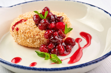 baked camembert with cranberry jam and mint leaves at white wooden table top. fried camembert with berry sauce is traditional french cuisine dessert