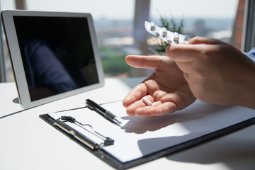 Woman sitting by the desk in the office and taking medical pills
