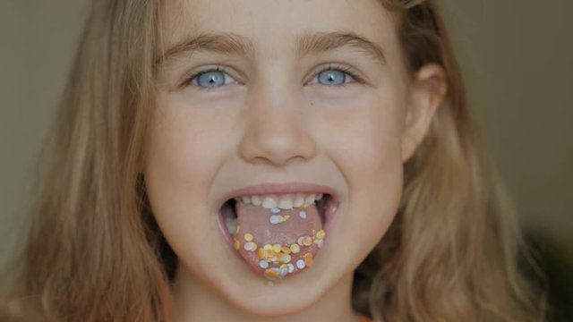 A child is smiling with a mouth full of candy. Little girl eating candy. Child eating chicle. Close up portrait silly girl with wavy hair sticking out tongue shaped candy pieces on tip.