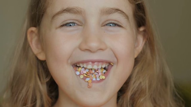 A child is smiling with a mouth full of candy. Little girl eating candy. Child eating chicle. Close up portrait silly girl with wavy hair sticking out tongue shaped candy pieces on tip.