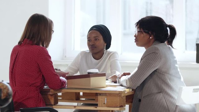 Female multiethnic company boss business woman talking to two African women at modern office table. Healthy workplace.