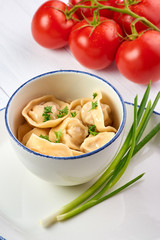 dumplings with parsley and onion at white wooden table top. Pelmeni - traditional russian cuisine dish dough with minced meat inside. decorated with tomatoes