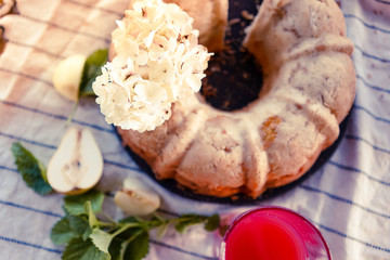 Homemade apple and pear pie charlotte decorated with hydrangea flower on a striped tablecloth on summer picnic.