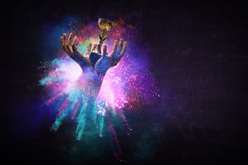 Hands holding champion cup on colourful splashes background. Mixed media