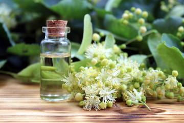 Linden essential oil bottle with fresh linden flowers on wooden