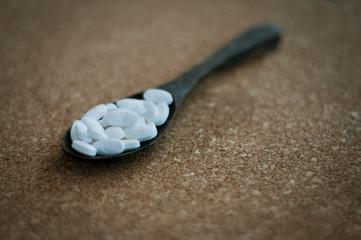 White pharmaceutical pills and medicines in the wooden spoon on a brown cork background....
