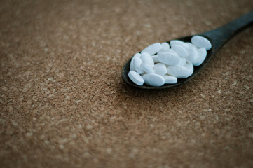 White pharmaceutical pills and medicines in the wooden spoon on a brown cork background. Valentines, heart, sick, health, and healing concept.