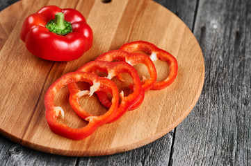 Sliced vegetable pepper close-up against the background of an old chopping board. Sweet low-calorie product. Pepper chopped with rings.
