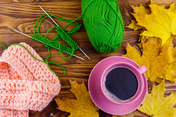 Cup of coffee, ball of yarn, knitting, knitted scarf and yellow maple leaves on wooden table. Autumn still life
