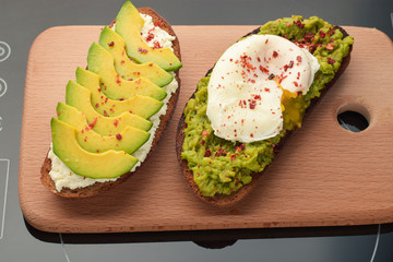 Avocado toasts with cheese and poached egg on a wooden cutting board