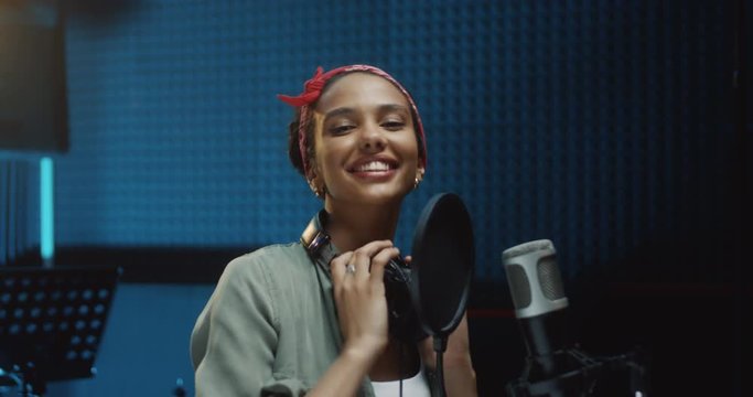 Close up of the young atractive and happy Caucasian young girl singer taking off headphones and smiling to the camera after finishing recording a song in the sound studio. Portrait shot.