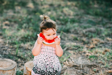 Charming girl year and a half, eating watermelon outdoors, in the village against the trees