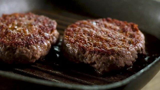 two meat fat juicy burgers with crispy brown crust are fried on a hot grill pan. heated Boiling hot butter splatters. Panoramic slow motion picture of the Cooking process in the kitchen.
