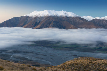 The valley is flooded in mist in a mountain environment. Over the fogs, only the high peaks of the mountains rise beneath the sunny sky. Misty morning. Beuatiful landscape concept.