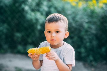 cute boy in the garden or Park outdoors eating boiled corn is very appetizing
