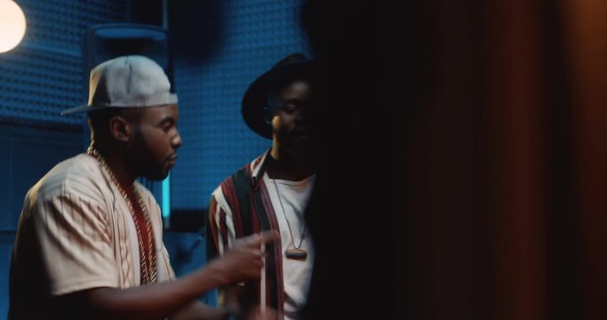 African American young handsome male two rappers recording a song in the dark sound studio and reading rap in the microphone.