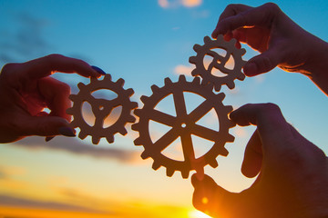 hands of businessmen assemble a puzzle from gears against the sky in the sunset. business concept idea, partnership, innovation, teamwork, cooperation